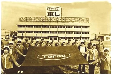新社名「東レ」のもと、社旗を掲げる社員(1971年頃)。社旗のマークは1963年5月より社章として使用